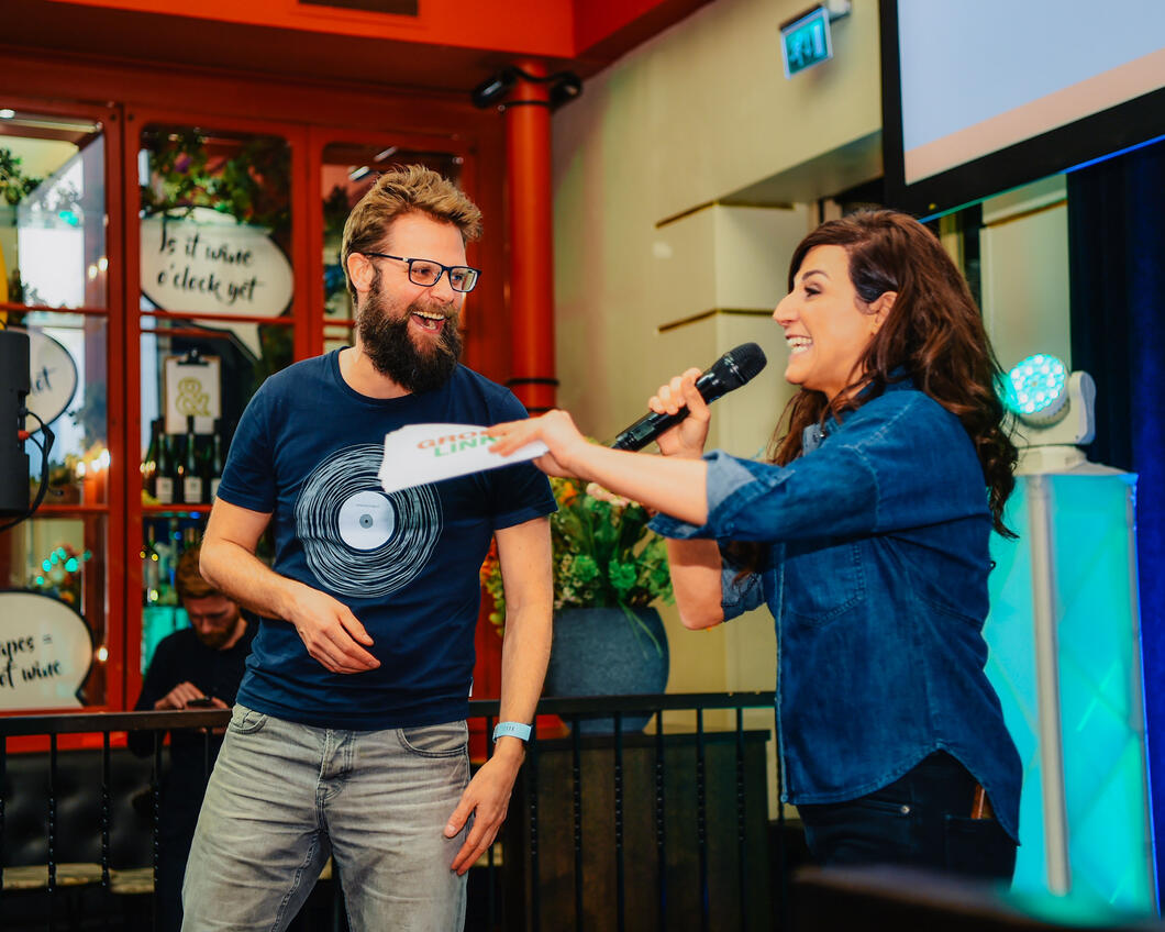 Raadsleden Bastiaan Bouwman en Melody Deldjou Fard presenteren met elkaar op het podium van een lokaal evenement.